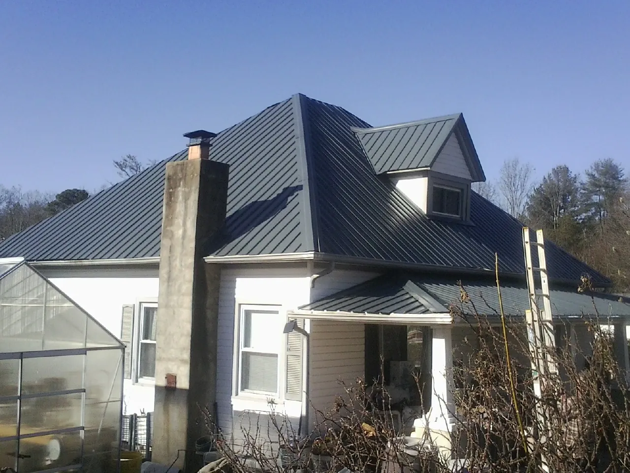 Dark blue standing seam metal roof on a white farmhouse with dormer — Slate & Tile Roof Repair by Roofing Brothers in Aydlett