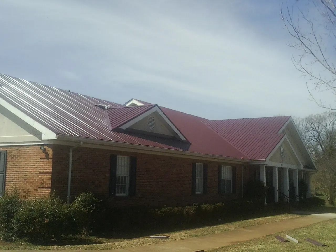 Red metal roof with gabled entries on a long brick building, from a Hail Damage Roof Repair job in Aydlett