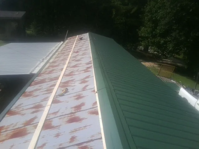 Old rusted panels beside newly installed green metal roofing — Wind Damage Roof Repair by Roofing Brothers in Aydlett
