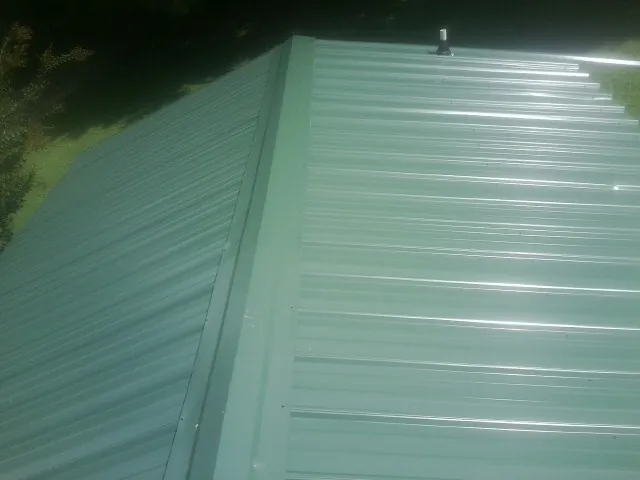 New green metal panels meeting at the ridge of a roof — Flat Roof Repair work by our crew in Aydlett