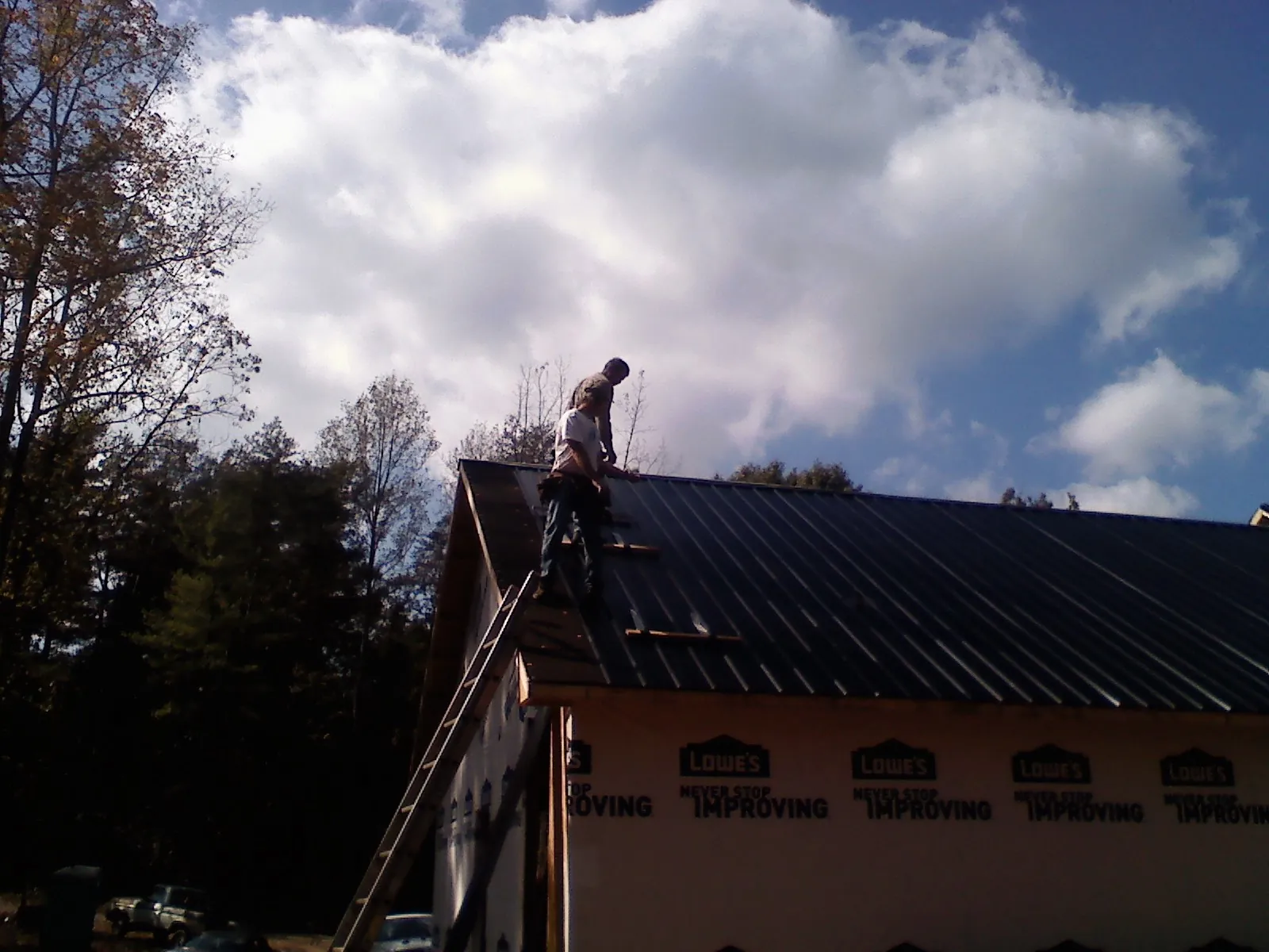 Roofer fastening dark metal panels high against a cloudy sky, from a Roof Inspection job in Aydlett