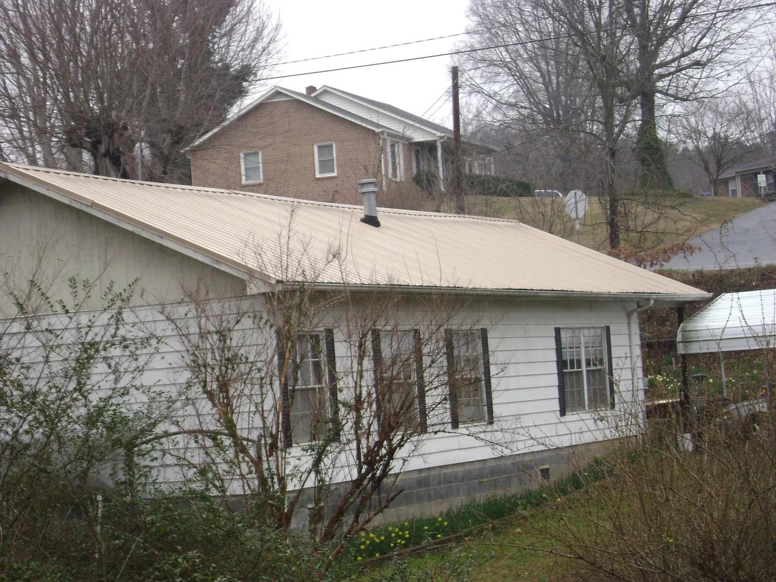 Tan metal roof on a white sided house set into a hillside — Commercial Roofing by Roofing Brothers in Aydlett
