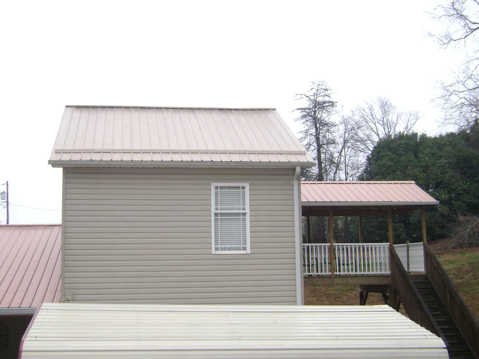 Tan metal roofs on a two story addition and attached porch, from a Roof Replacement job in Aydlett